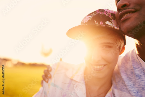 Mixed race couple of millennials in a grass field cuddling and showing affection together