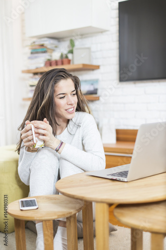 Young beautiful woman sitting on the floor working on laptop. Morning scene