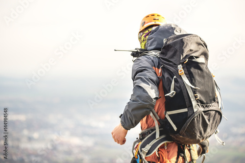 Close-up of a climber from the back in gear and with a backpack with equipment on the belt, stands on a rock, at high altitude