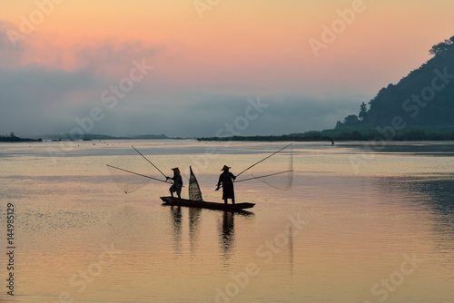 Silluate fisherman and boat in river on during sunrset,fisherman trowing the nets on during sunset,during sunset,Thailand © saravut