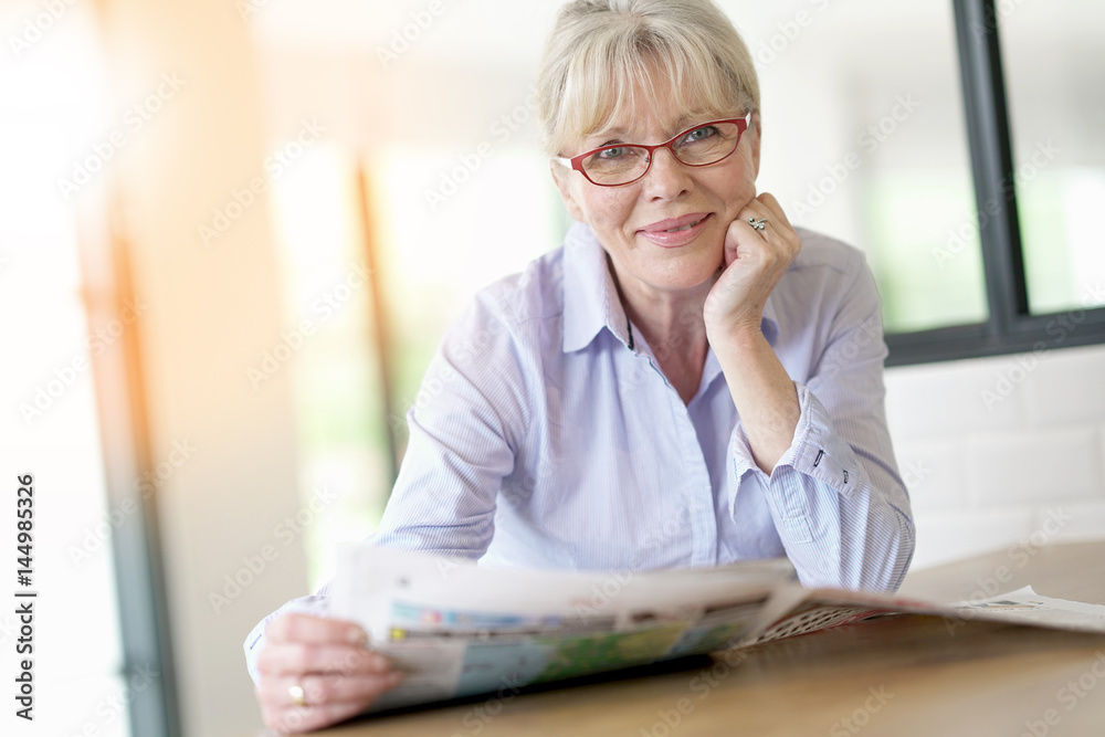 Senior woman with eyeglasses reading newspaper at home Senior woman with eyeglasses reading newspaper at home