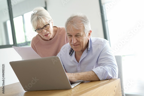Senior couple at home connected on internet with laptop