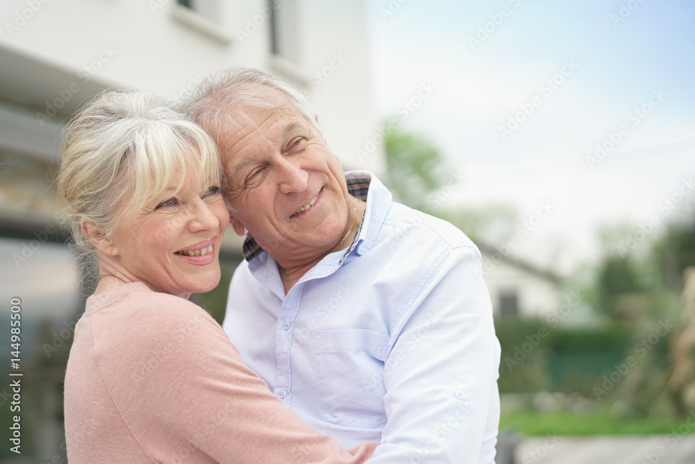 Senior couple embracing in front of new modern house
