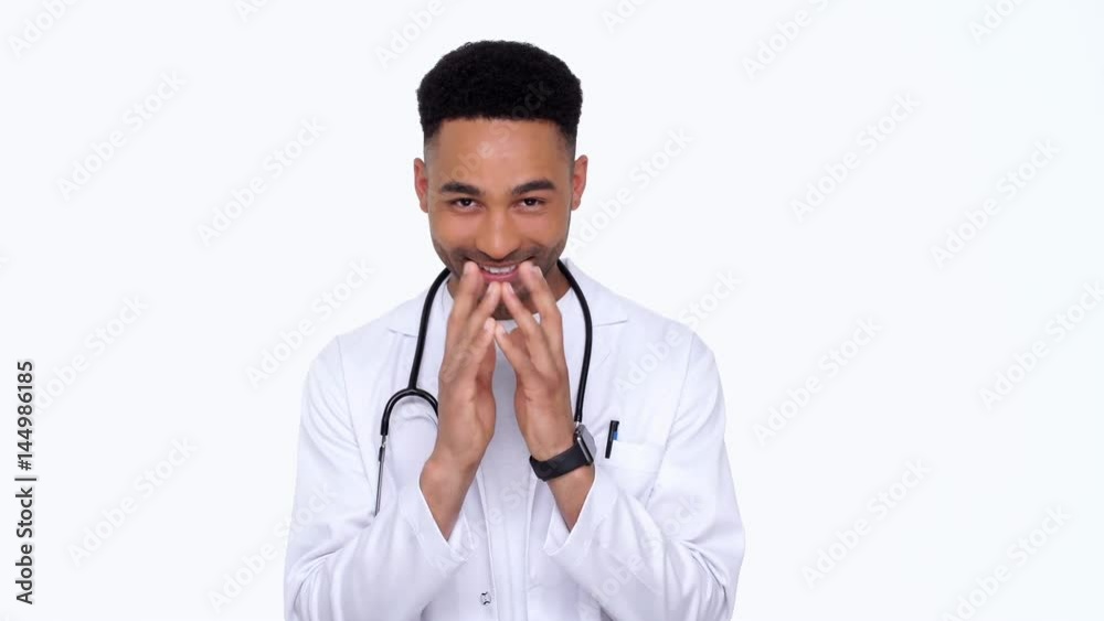 Wily young doctor wearing white lab coat fingering over and smiling isolated Wily young doctor wearing white lab coat fingering over and smiling isolated