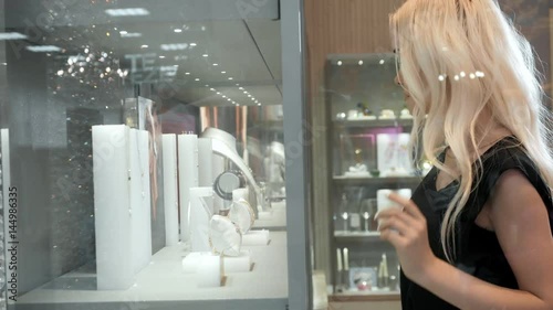 Young woman looking at the shop showcase and jewelry to look at it closer, beautiful student blonde fashion model in juwellery mall shopping photo