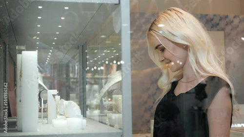 Young woman looking at the shop showcase and jewelry to look at it closer, beautiful student blonde fashion model in juwellery mall shopping photo