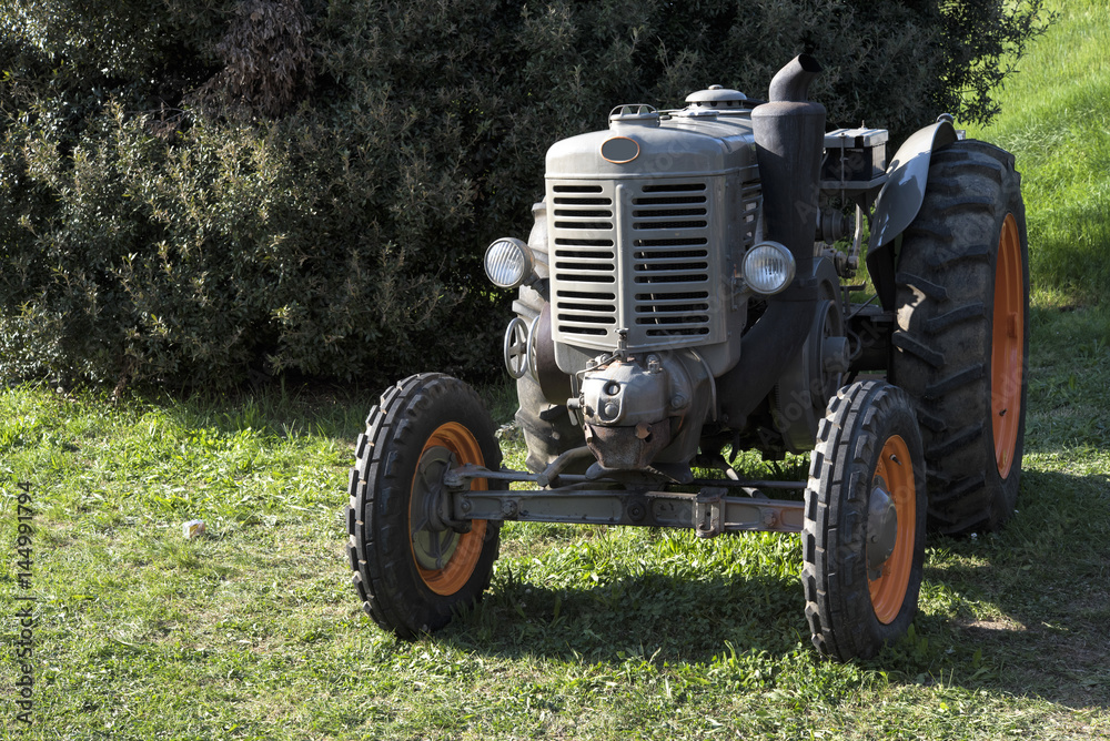 An old orange and green retro tractor in a field. An old orange and green retro tractor in a field.