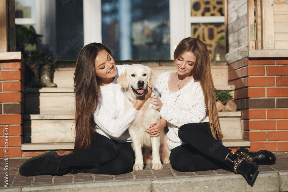 Obraz premium Young,beautiful women with long, straight,blond hair, beautiful smiles,are dressed in black leggings,posing outdoors in the spring,sitting in the city with their friend,dog,breeds a golden retriever