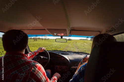 A young couple travels to shirts and shorts, sitting in the car. Tourists go on the jeep next to the grass staring at the horizon. With space for your text. Travel and adventure concept.