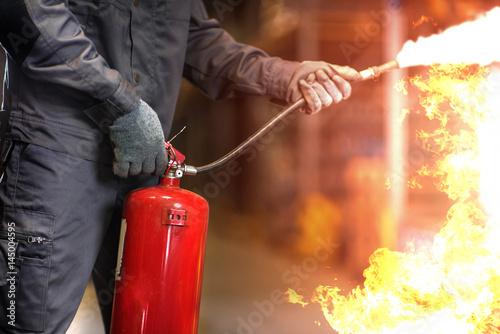 Man using fire extinguisher fighting fire closeup photo. #145004595