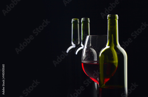 Bottles and glass of red wine on a black background .