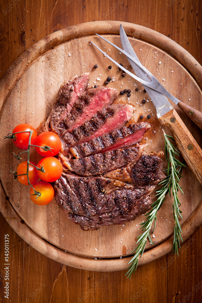 Sliced medium rare grilled Beef steak Ribeye with cherry tomatoes on cutting board, selective focus