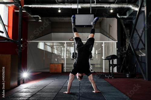 Athlete walking on his hands standing upside down in gym. Man doing push ups on his hands. Crossfit training. Workout lifestyle concept