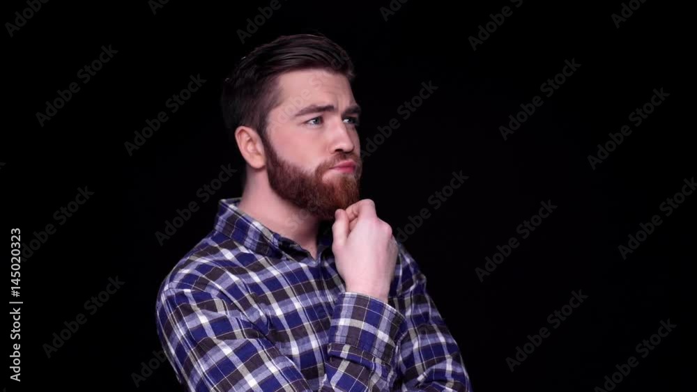 Pensive young bearded man thinking with hand on his chin and looking away isolated over black Pensive young bearded man thinking with hand on his chin and looking away isolated over black