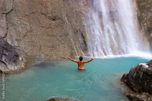 Young men joys his deep in turquoise waterfall in mountains with