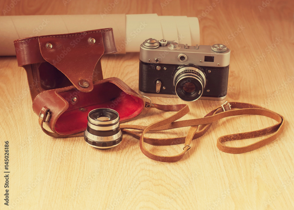 Old camera, lens and leather case on wooden background in vintage style.