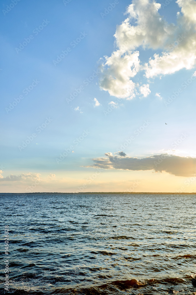 Beautiful sea, river, lake, reservoir. Natural panorama in the rays of the setting, the rising sun. A magnificent blue sky with neat clouds. 