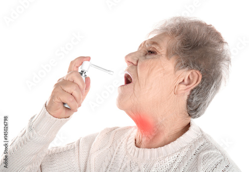 Allergies and sore throat concept. Sick senior woman using spray on white background