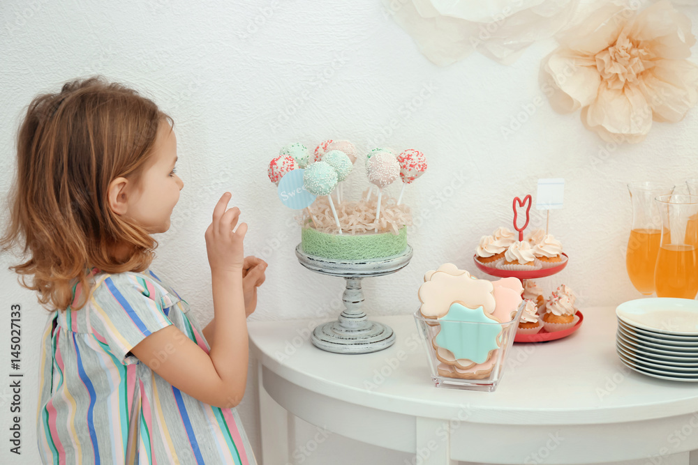 Cute girl near table with sweets served for party