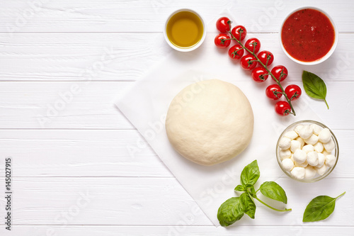 Raw pizza dough with ingredients: mozzarella, tomatoes sauce, basil, olive oil, cheese, spices. Italian margherita on wooden table. Italian pizza margarita