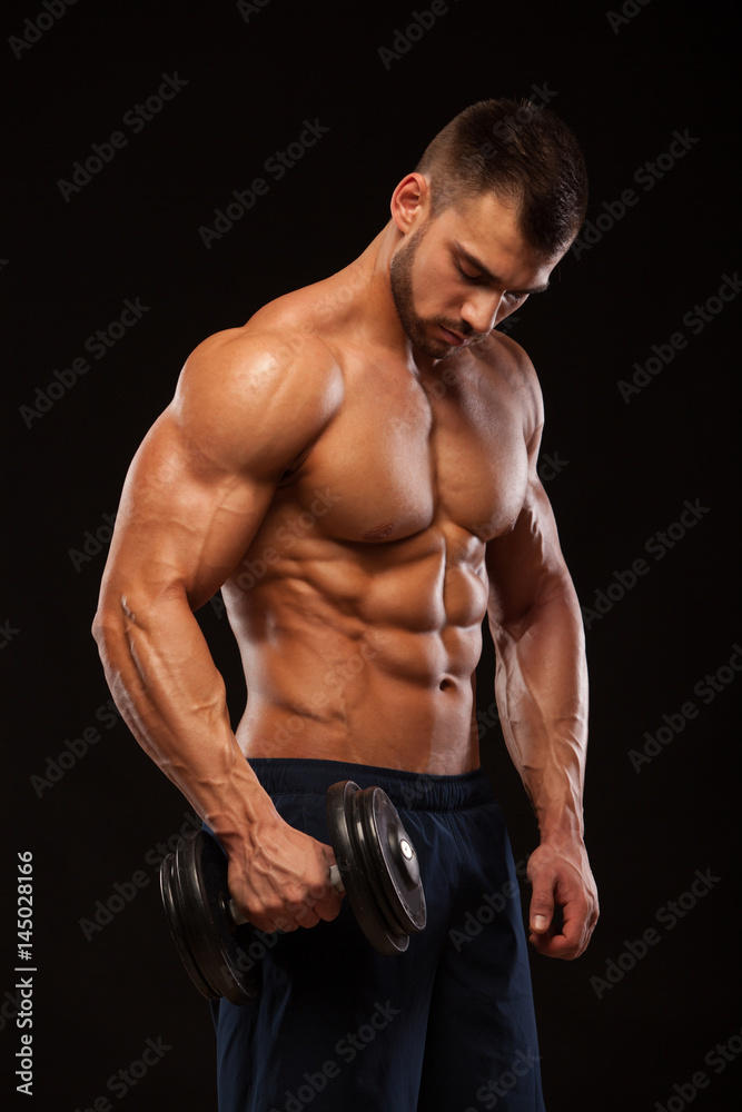 Handsome power athletic man with dumbbell is confidently looking forward. Strong bodybuilder with six pack, perfect abs, shoulders, biceps, triceps and chest Isolated on black background with