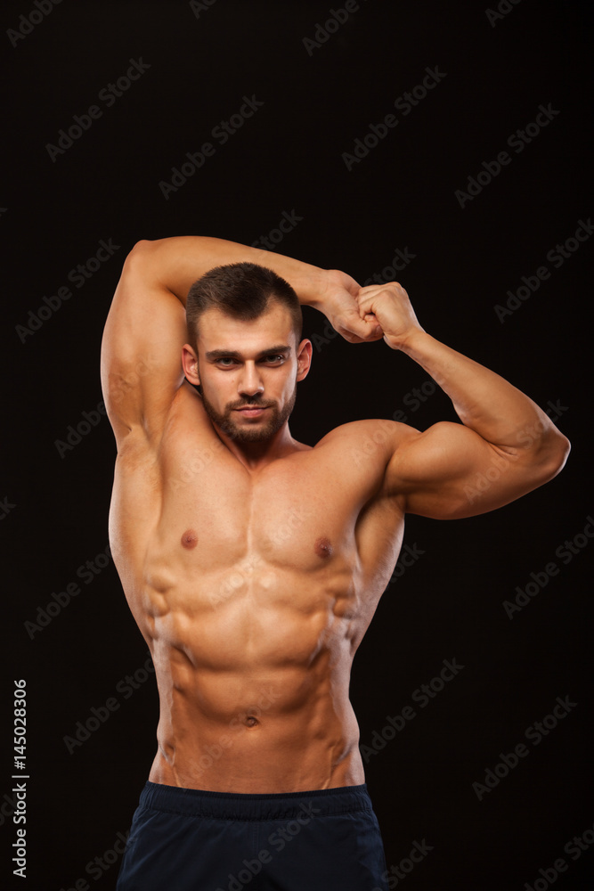 Strong Athletic Man - Fitness Model is showing his Torso with six pack abs and holding his hands up. isolated on black background with copyspace