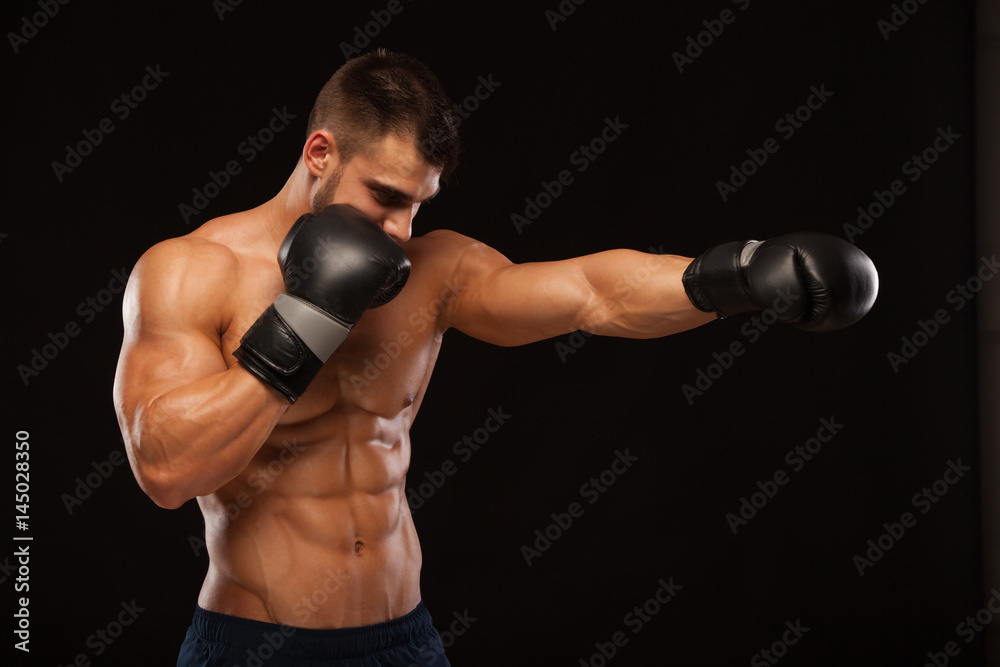 Muscular young man with perfect Torso with six pack abs, in boxing gloves is showing the different movements and strikes isolated on black background with copyspace