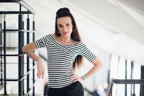 Designer of fashion clothes posing and looking at the camera in a cafe with huge windows behind her. Sexy beautiful woman wearing stylish striped blouse shirt.