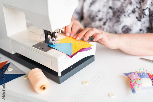 patchwork and quilting in the workshop of a tailor woman on white background - close up on tailor hands and sewing machine with scraps of blue and yellow fabric for patchwork