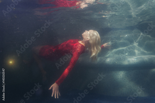 Blonde woman in a red dress under the water.