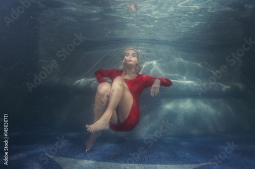 Woman dives under the water in a red dress.