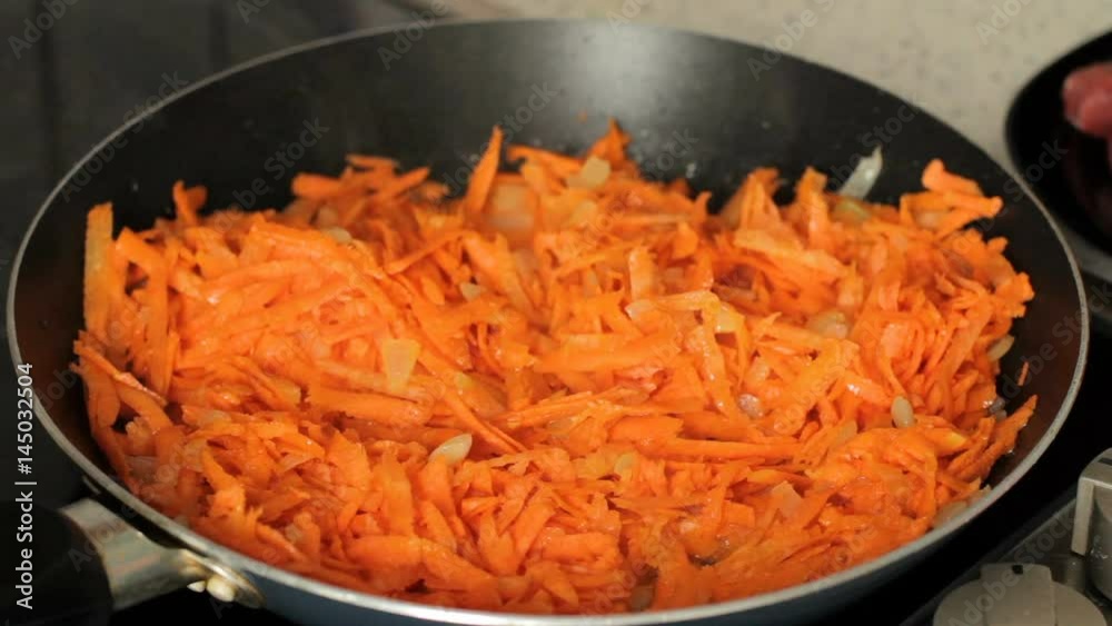 Grated carrots are fried on a frying pan. There is steam from carrots with onions when frying. Close-up Grated carrots are fried on a frying pan. There is steam from carrots with onions when frying. Close-up