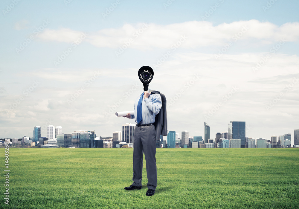 Camera headed man standing on green grass against modern citysca Camera headed man standing on green grass against modern citysca