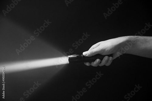 The flashlight in the man's hand from the right side of the frame in black and white color isolated on black background