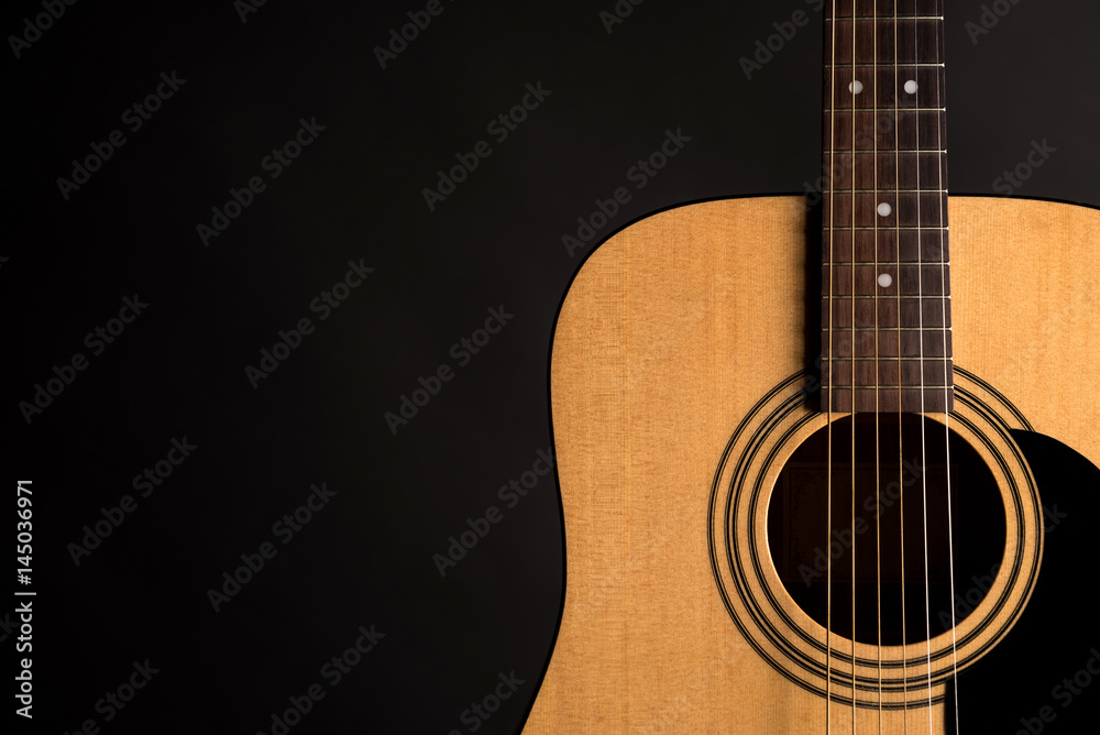 Obraz premium Part of a wooden acoustic guitar on the right side of the frame, on a black isolated background