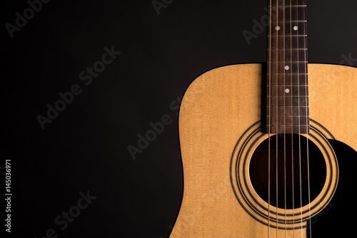 Part of a wooden acoustic guitar on the right side of the frame, on a black isolated background