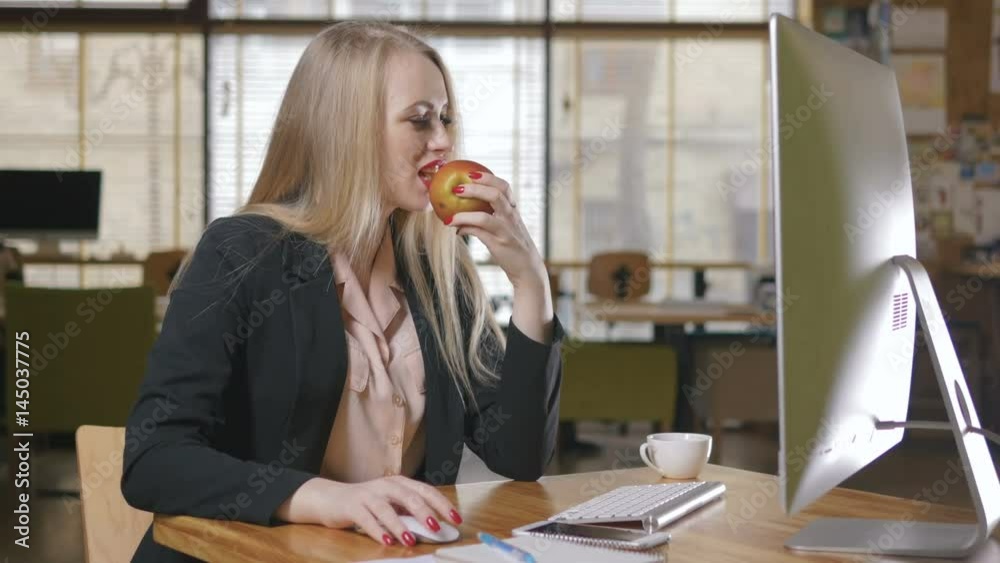 Portrait of pretty young woman eating an apple in her office.