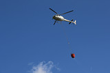 Helicopter picking up  and carrying water during fire fighting operations against blue skies
