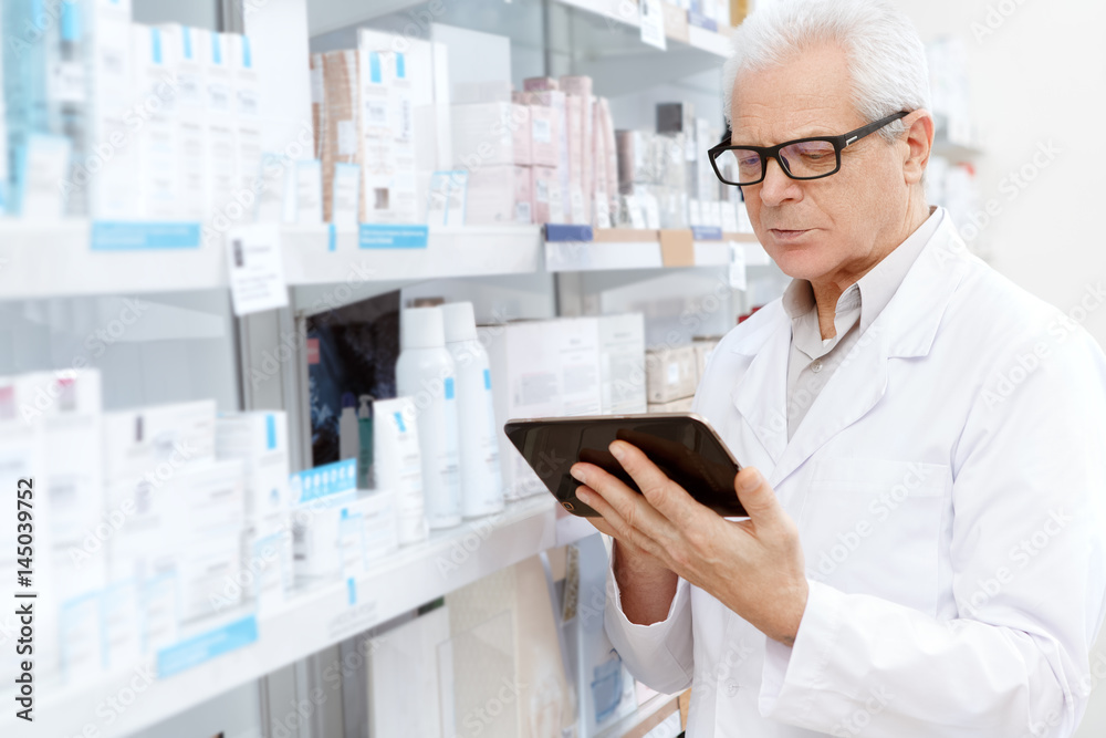 Elderly male pharmacist using digital tablet at work Elderly male pharmacist using digital tablet at work