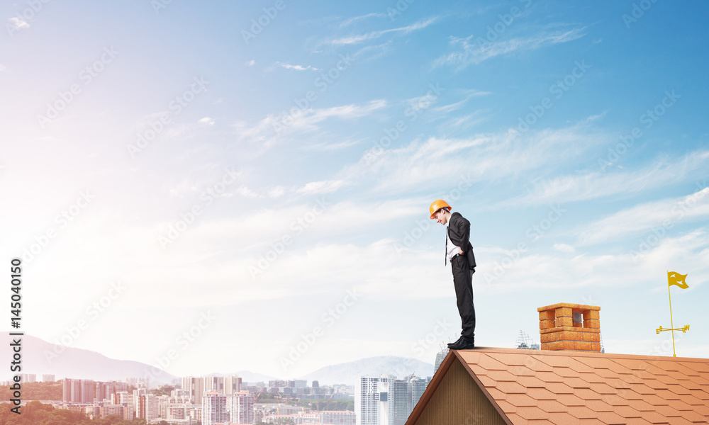 Businessman looking down from roof and modern cityscape at background. Mixed media Businessman looking down from roof and modern cityscape at background. Mixed media