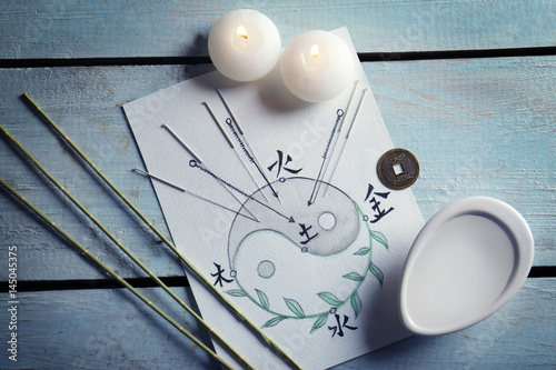 Acupuncture needles with candles and drawing on wooden background