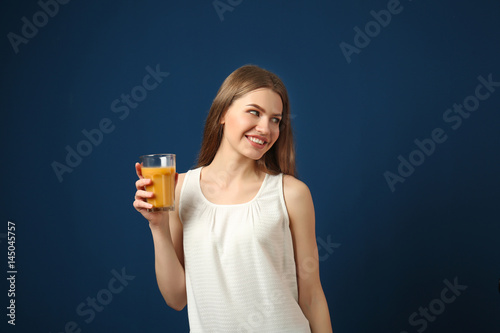 Beautiful young woman with glass of fresh juice on dark blue background