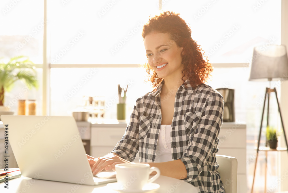 Beautiful young woman sitting at table and using laptop Beautiful young woman sitting at table and using laptop