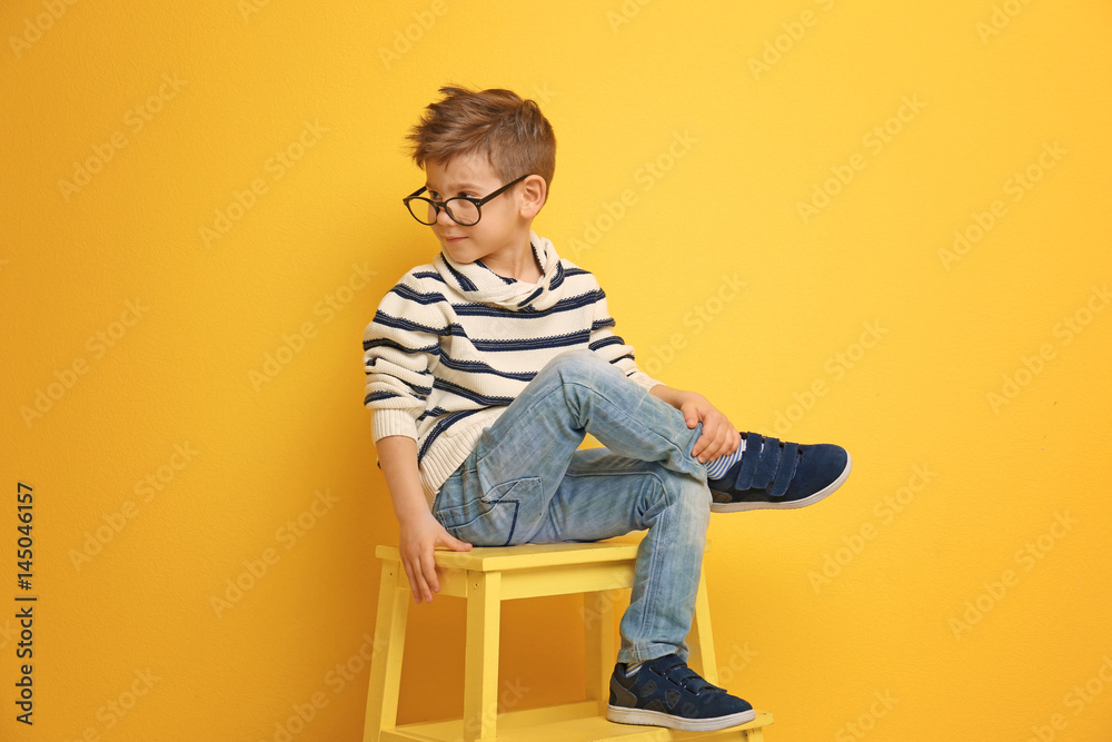 Cute stylish boy sitting on chair near color wall Cute stylish boy sitting on chair near color wall