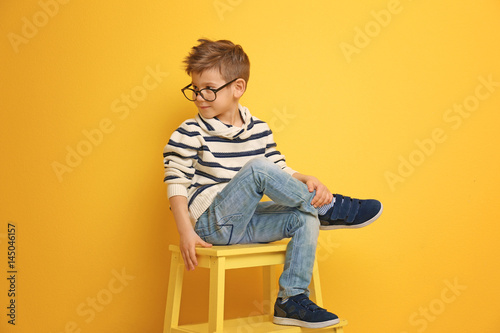 Cute stylish boy sitting on chair near color wall © Africa Studio