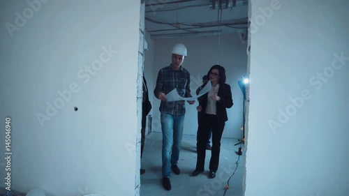 A taskmaster with investor and supervisor walking on a construction site with the plan and talking about interior