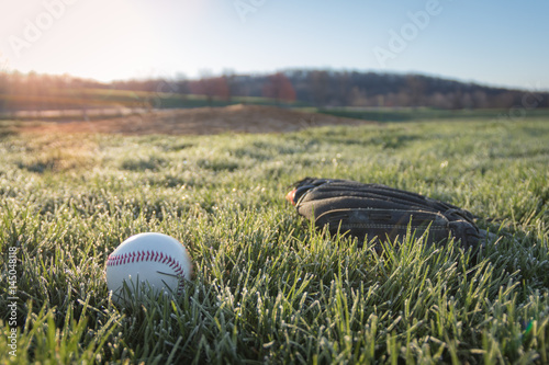 Photography Baseball glove and ball on field in early morning grass and dew as sun rises in