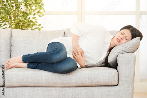 young woman suffering from stomachache on sofa