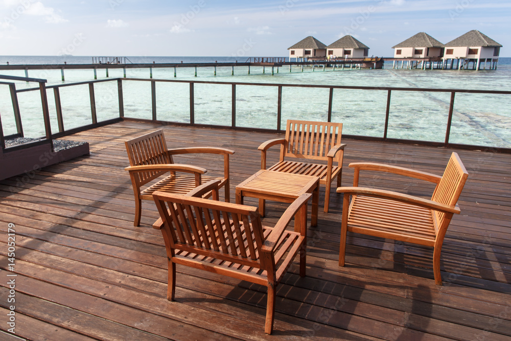 Wooden chairs at balcony with water villas background