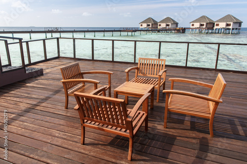Wooden chairs at balcony with water villas background